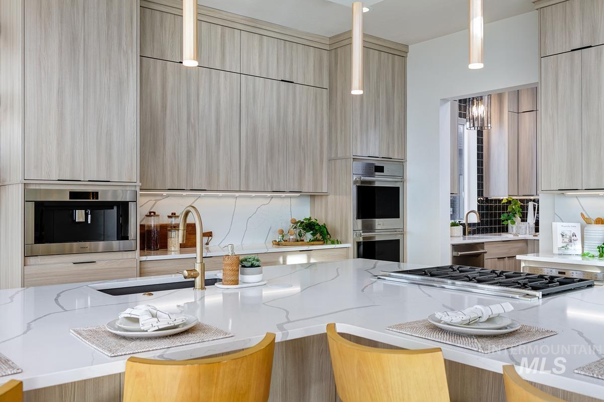 Kitchen featuring light stone countertops, light brown cabinetry, appliances with stainless steel finishes, modern cabinets, and pendant lighting