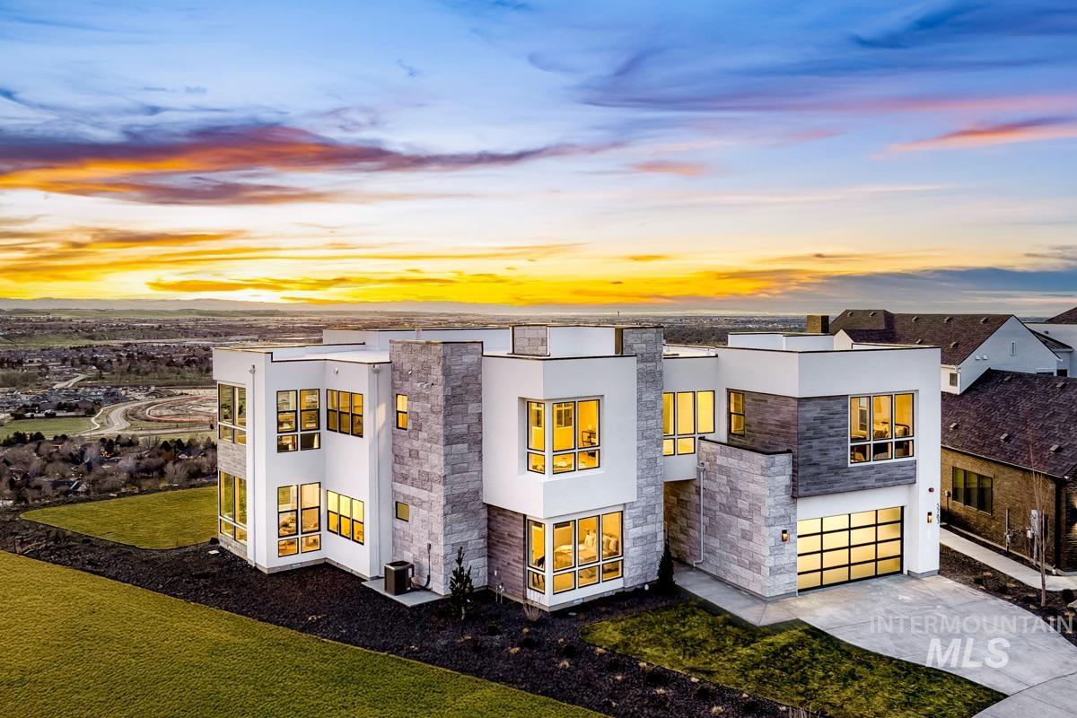 Back of house at dusk featuring stucco siding, stone siding, concrete driveway, and an attached garage