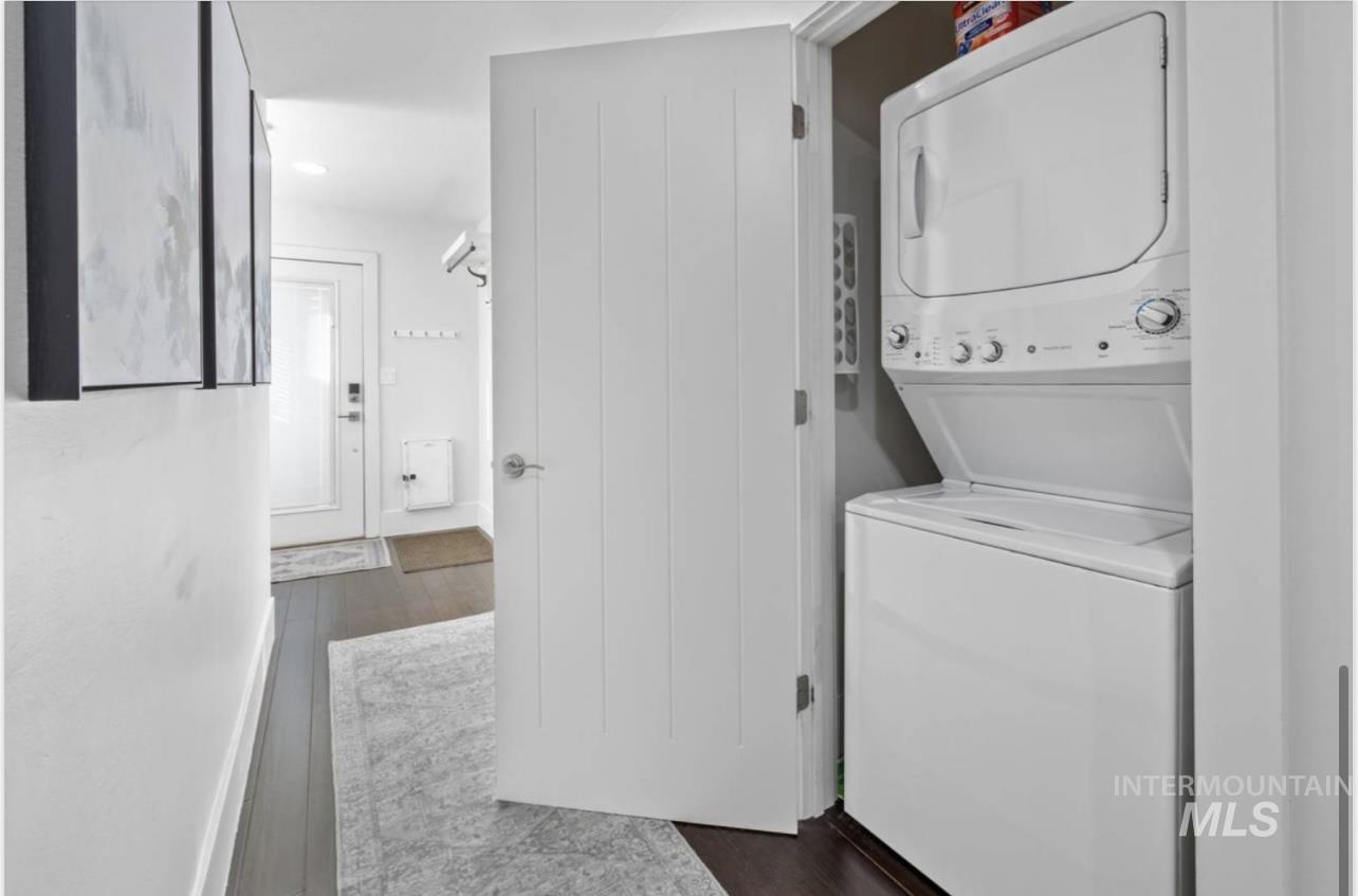 Laundry room with dark wood-style floors, stacked washer / drying machine, and recessed lighting
