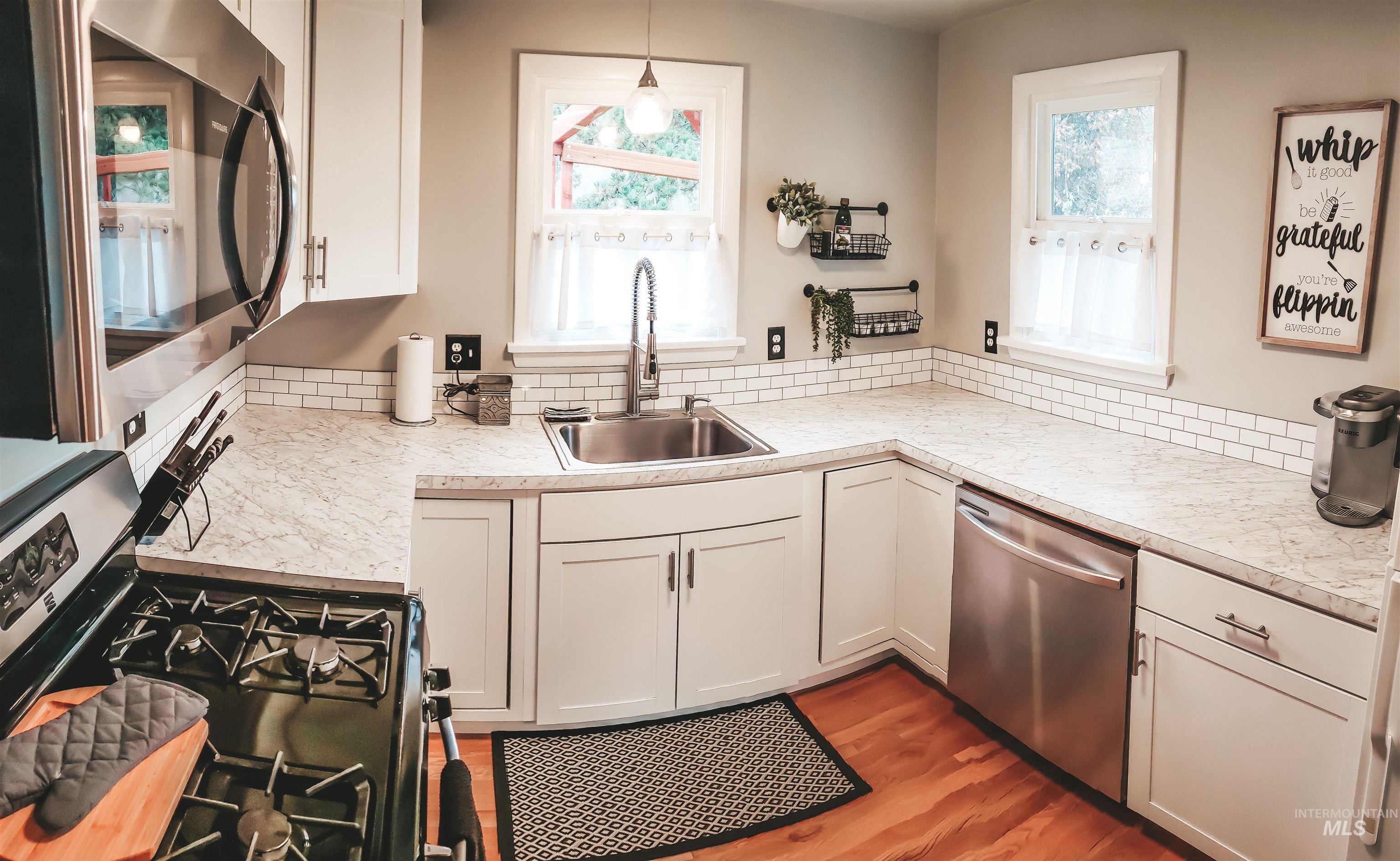 Kitchen featuring white cabinetry, light-toned countertops, a subway tile backsplash, and stainless steel appliances including a range and dishwasher