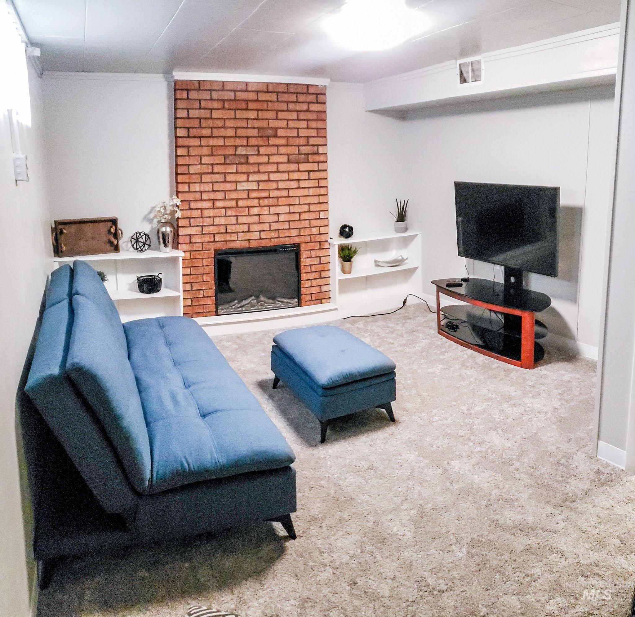 Living space featuring a brick-accented fireplace with electric insert, built-in shelving, light-toned carpeting, and recessed ceiling lighting