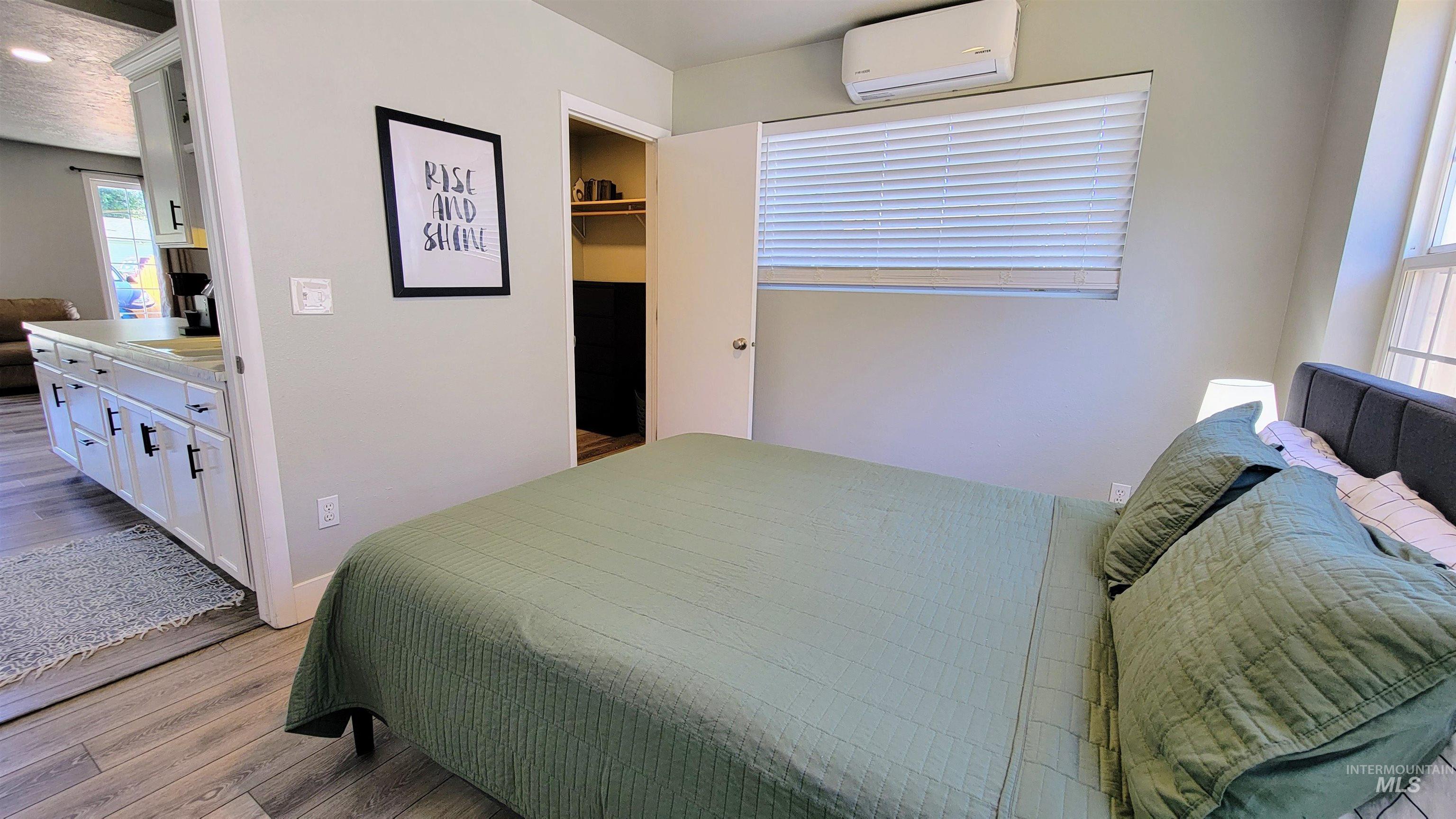 Bedroom featuring wood-finish flooring, a mini-split AC unit, a window with horizontal blinds, and an open closet