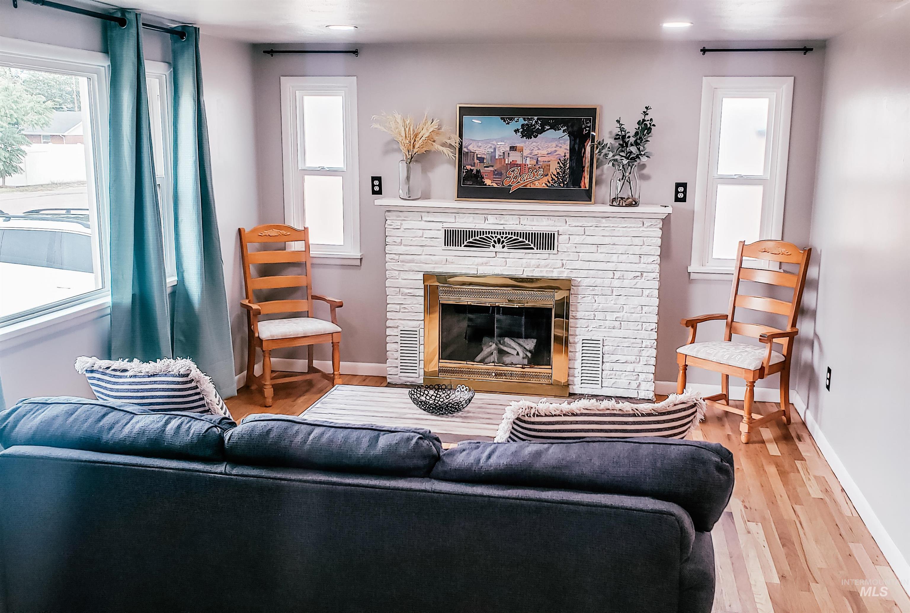 Living area featuring a white brick fireplace with a brass-trimmed insert, hardwood flooring, recessed lighting, and a dual-pane window