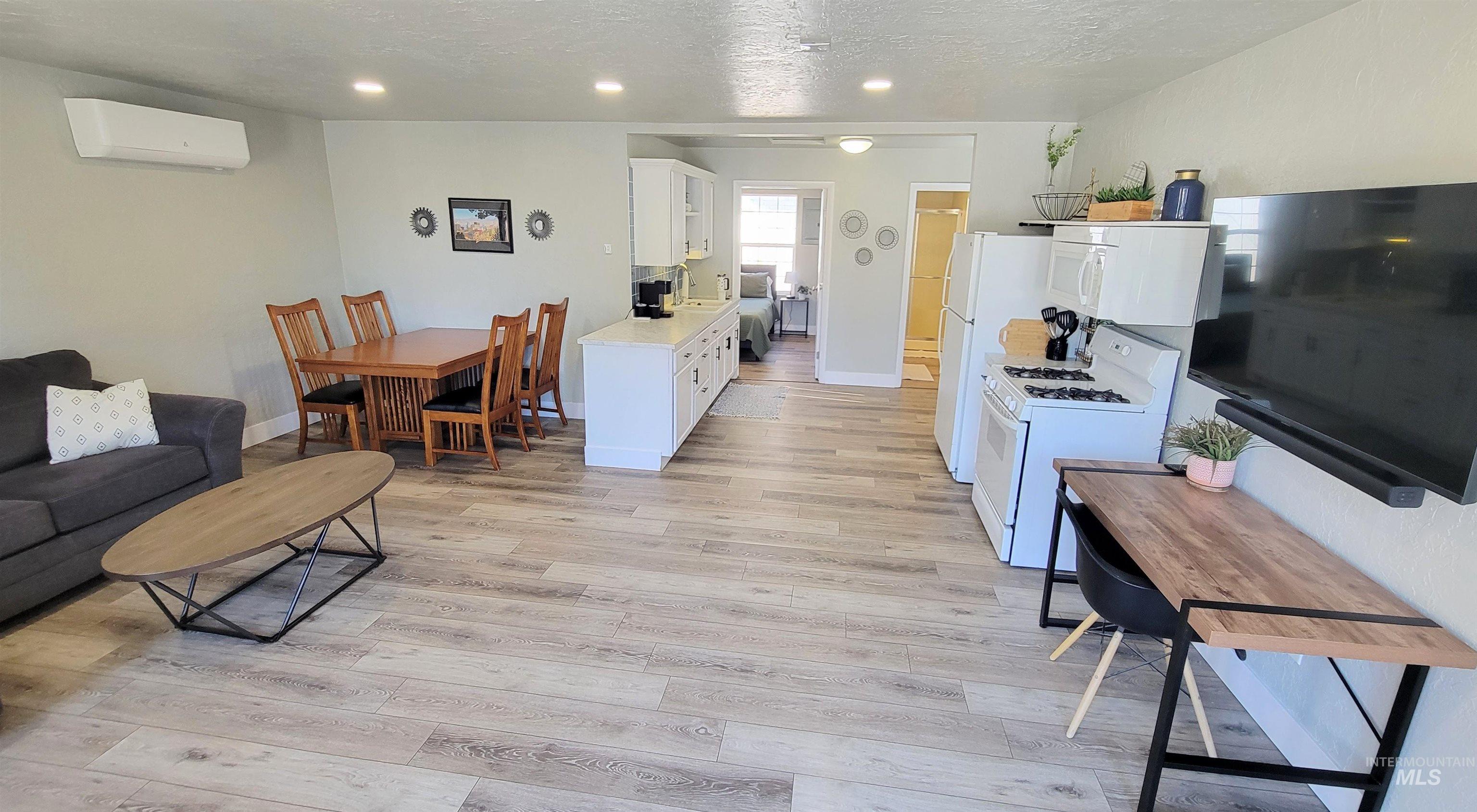 Open-concept living space featuring wood-finish flooring, recessed lighting, and a white kitchen with a gas range