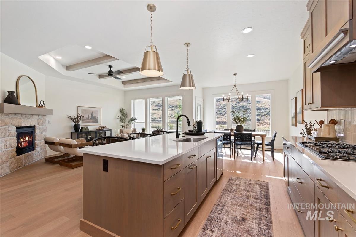 Kitchen with light wood-style floors, a stone fireplace, open floor plan, a ceiling fan, and a center island with sink