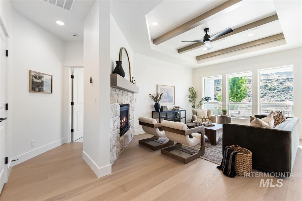 Living area featuring light wood-type flooring, a raised ceiling, a stone fireplace, a ceiling fan, and recessed lighting