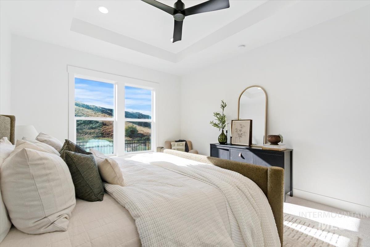 Carpeted bedroom with ceiling fan, a raised ceiling, and recessed lighting
