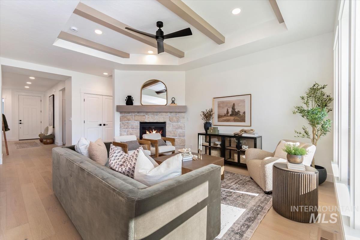 Living room featuring a tray ceiling, light wood-type flooring, a fireplace, a ceiling fan, and recessed lighting