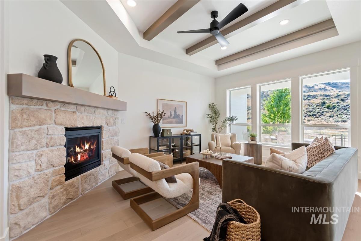 Living room with a stone fireplace, wood finished floors, a ceiling fan, recessed lighting, and a tray ceiling