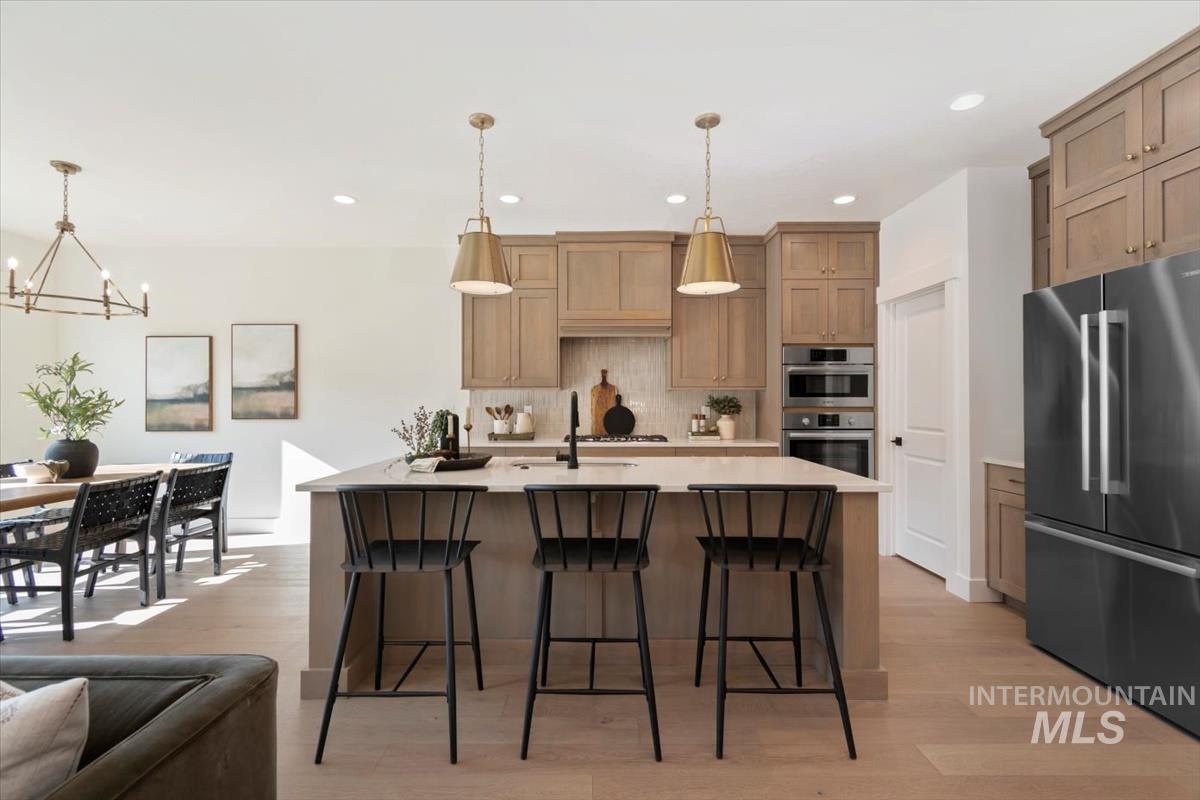 Kitchen with stainless steel appliances, light wood-type flooring, a breakfast bar, an island with sink, and suspended lighting
