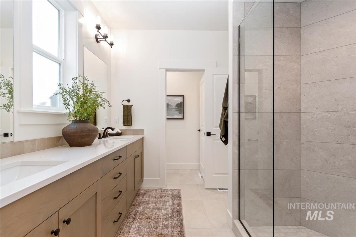 Bathroom with double vanity, light tile patterned floors, and a tile shower