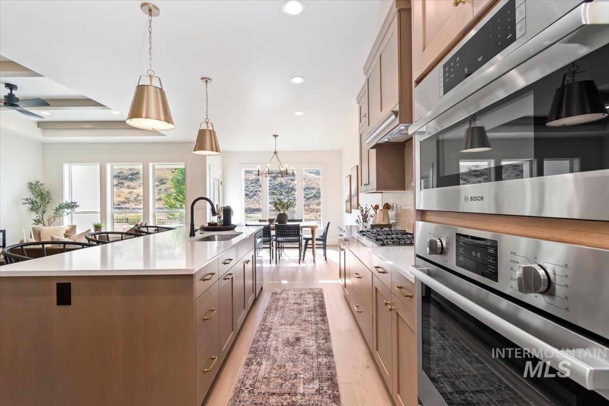 Kitchen with stainless steel appliances, a large island, light wood finished floors, light stone countertops, and decorative backsplash