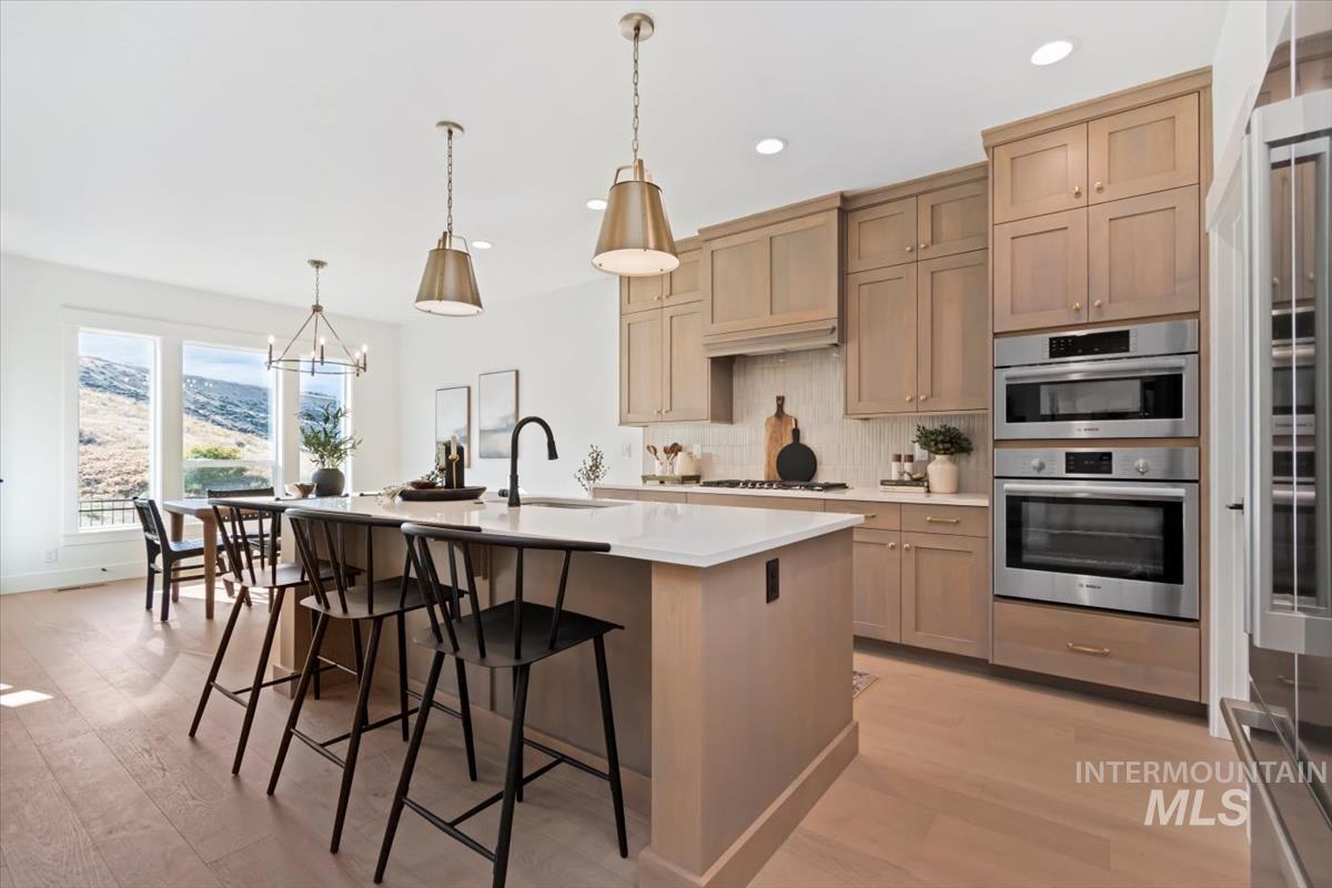 Kitchen featuring backsplash, light wood-style floors, a breakfast bar area, stainless steel appliances, and a kitchen island with sink