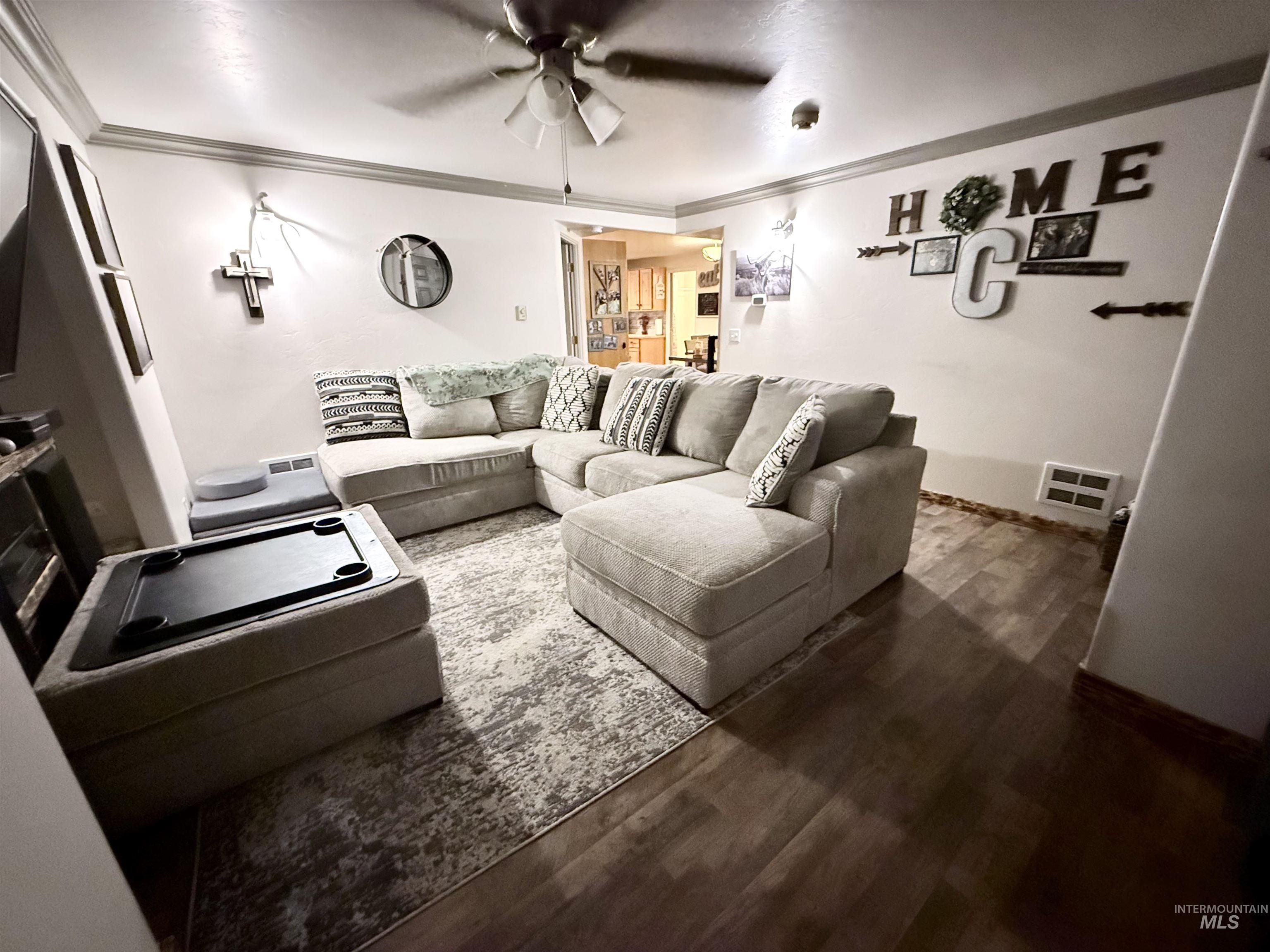 Living area featuring crown molding, dark wood-type flooring, and ceiling fan