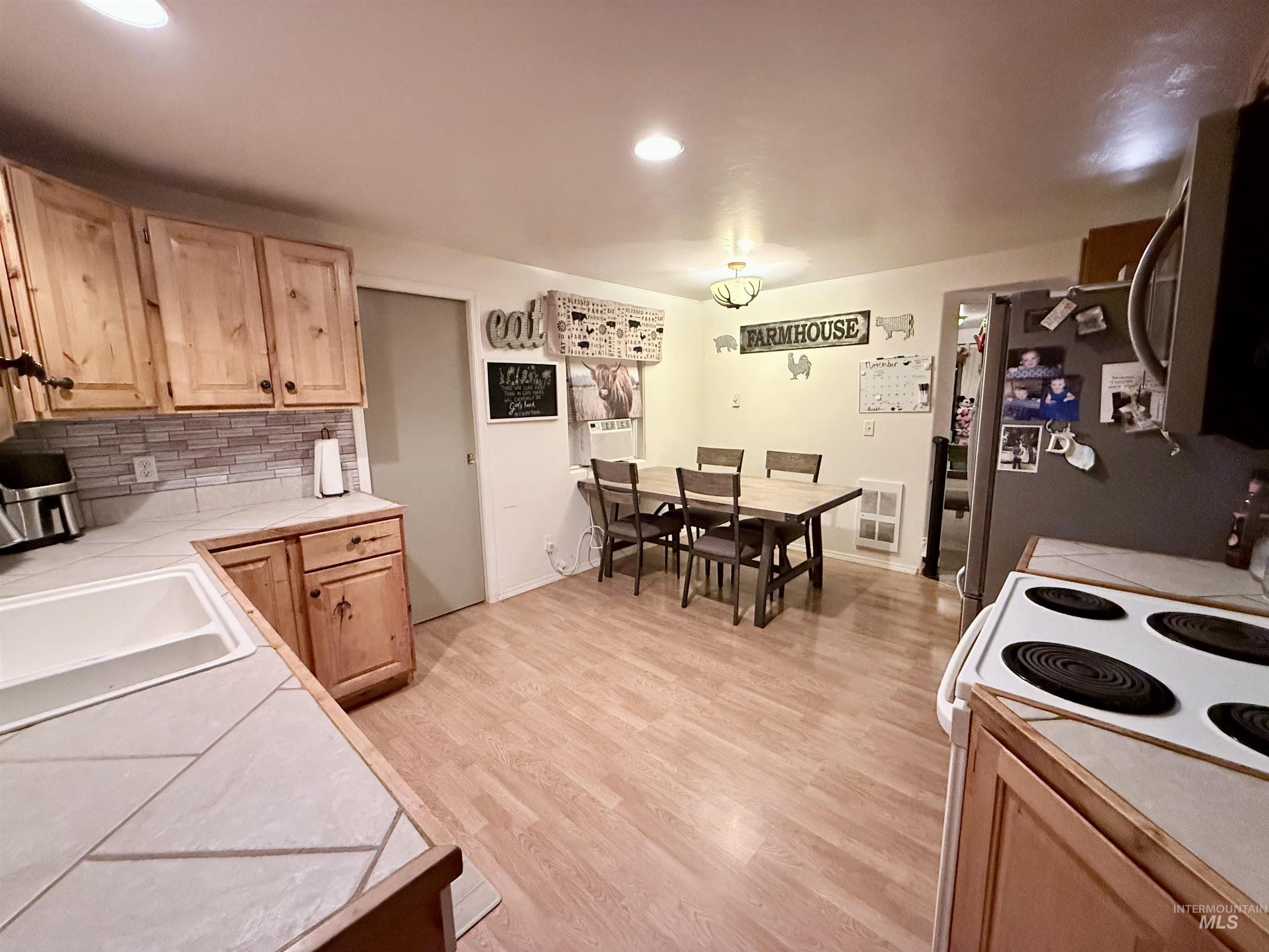 Kitchen with light brown cabinetry, backsplash, stainless steel appliances, light wood finished floors, and tile countertops
