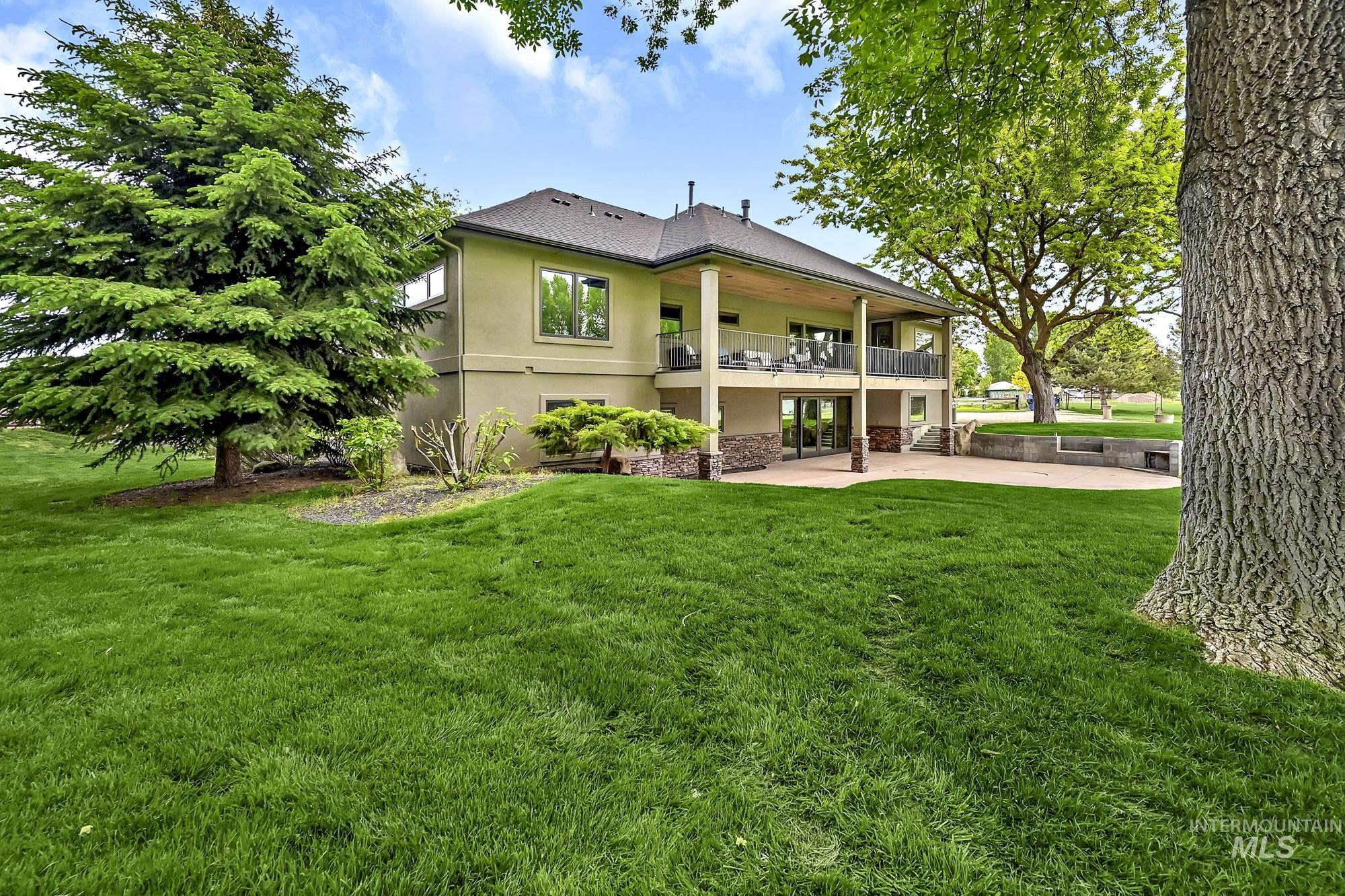 Rear view of property featuring stucco siding, a yard, a patio, a balcony, and stone siding