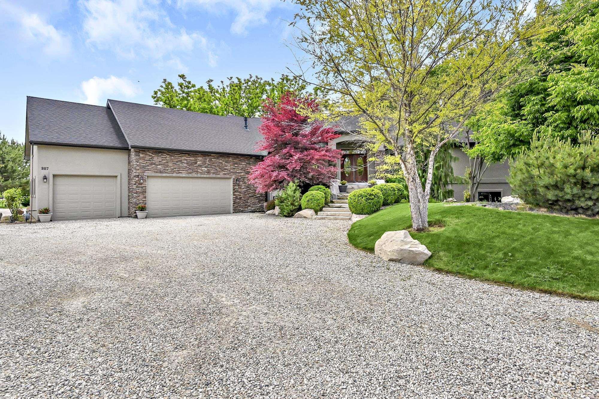 View of front of home featuring gravel driveway, stone siding, a garage, and front yard