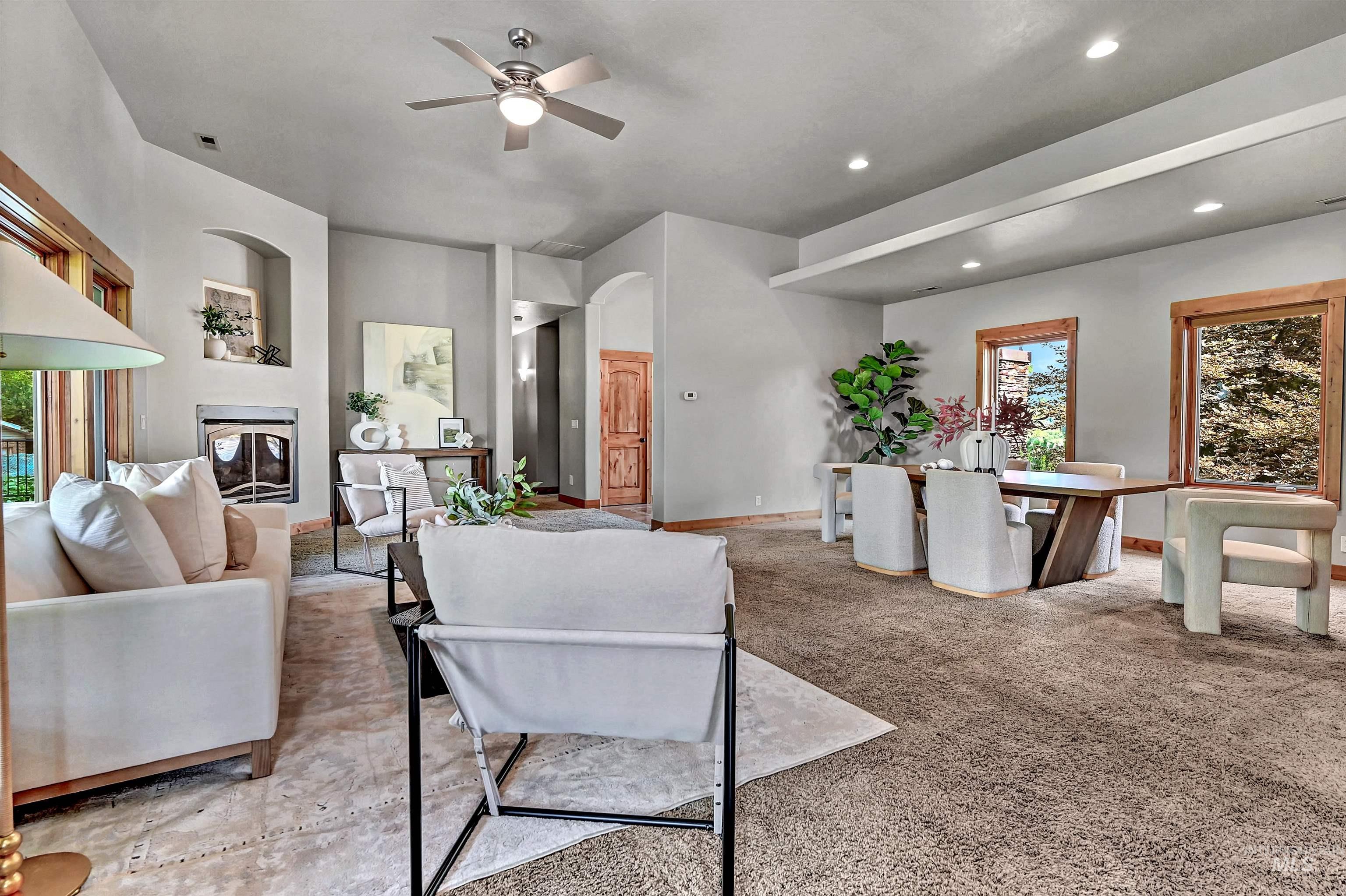 Living area with a glass covered fireplace, light colored carpet, ceiling fan, recessed lighting, and arched walkways