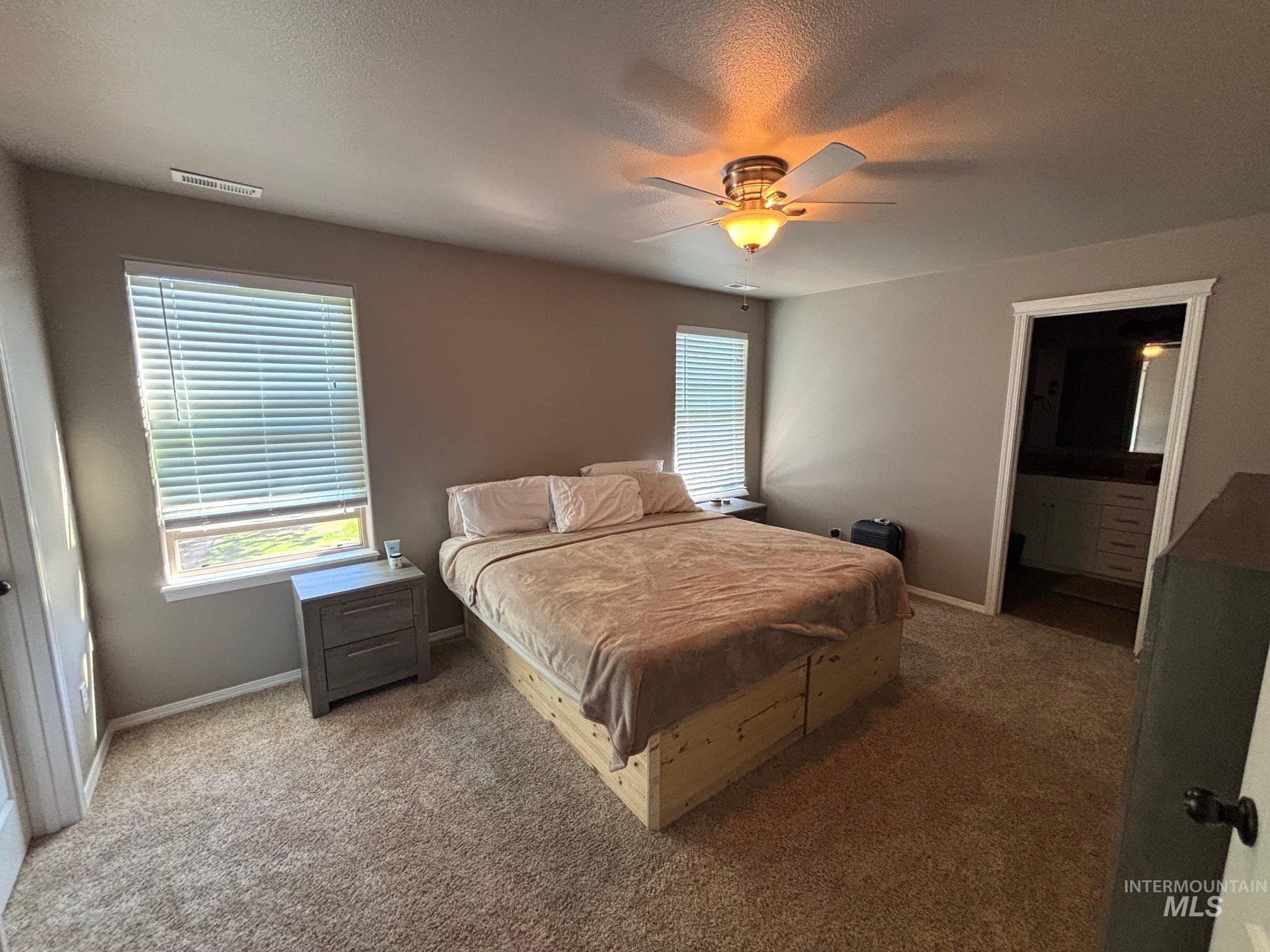 Carpeted bedroom featuring a textured ceiling, ceiling fan, and ensuite bathroom