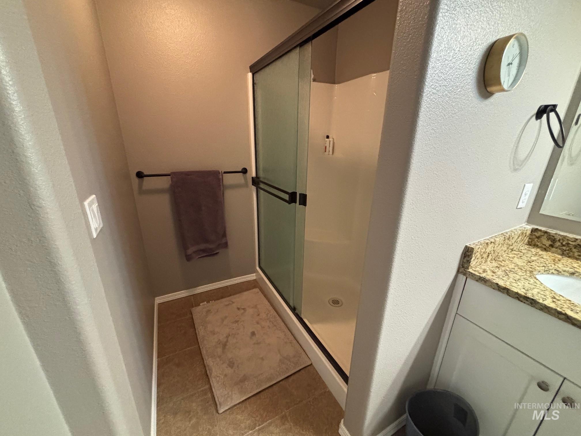 Bathroom featuring vanity, a shower stall, a textured wall, and light tile patterned flooring