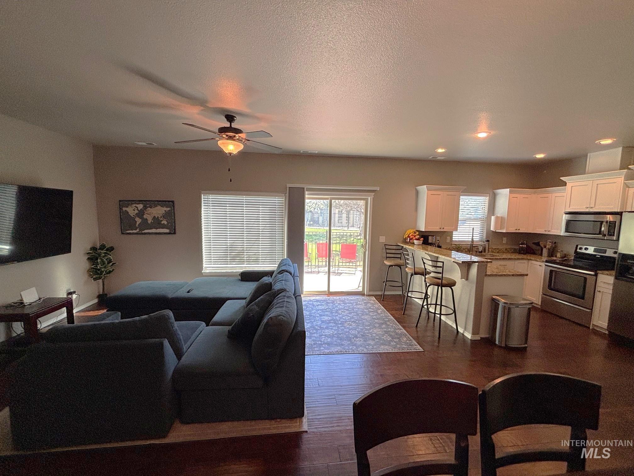 Living area with dark wood-type flooring, healthy amount of natural light, a ceiling fan, a textured ceiling, and recessed lighting
