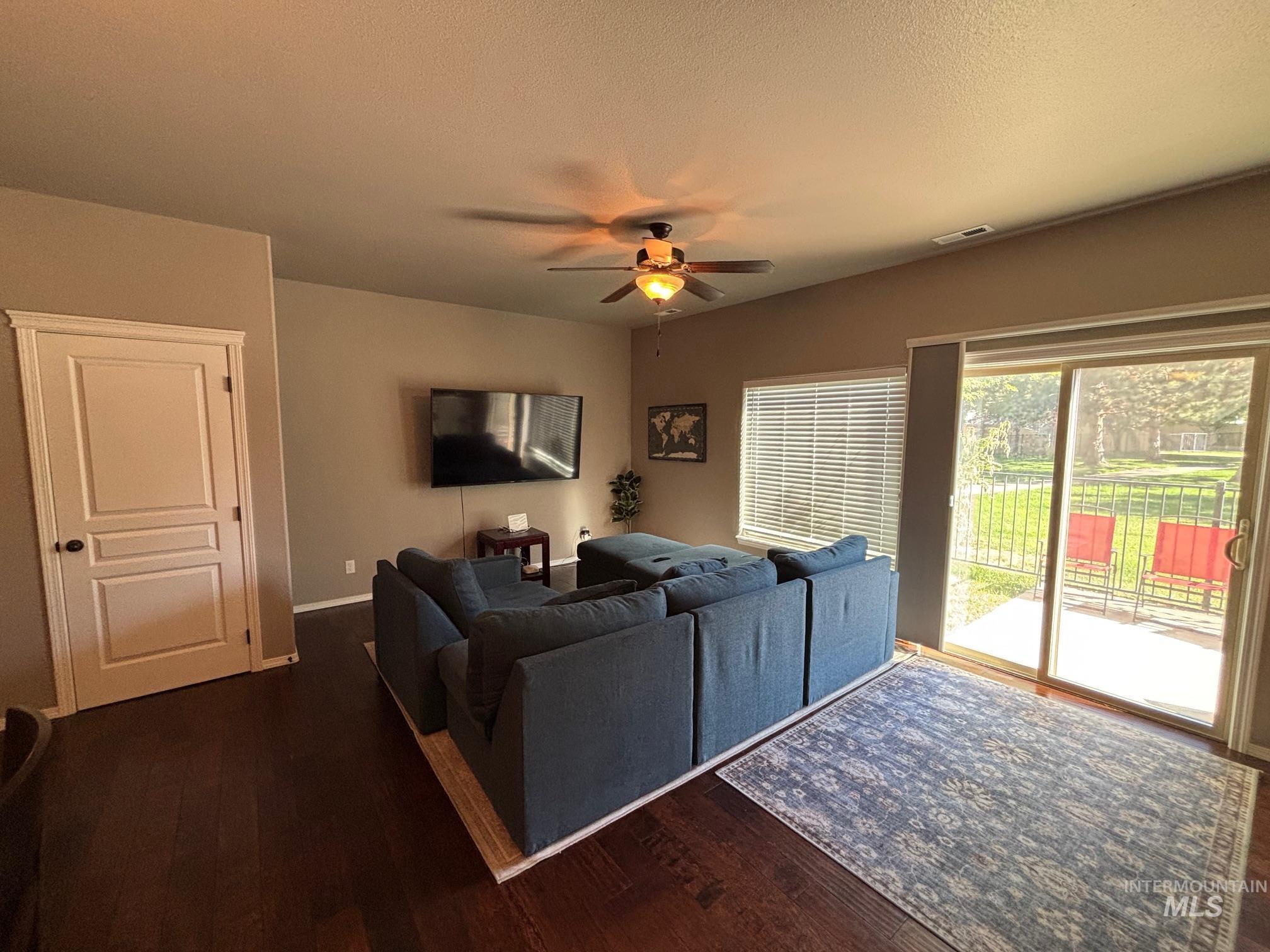 Living area with ceiling fan, dark wood-style flooring, and a textured ceiling