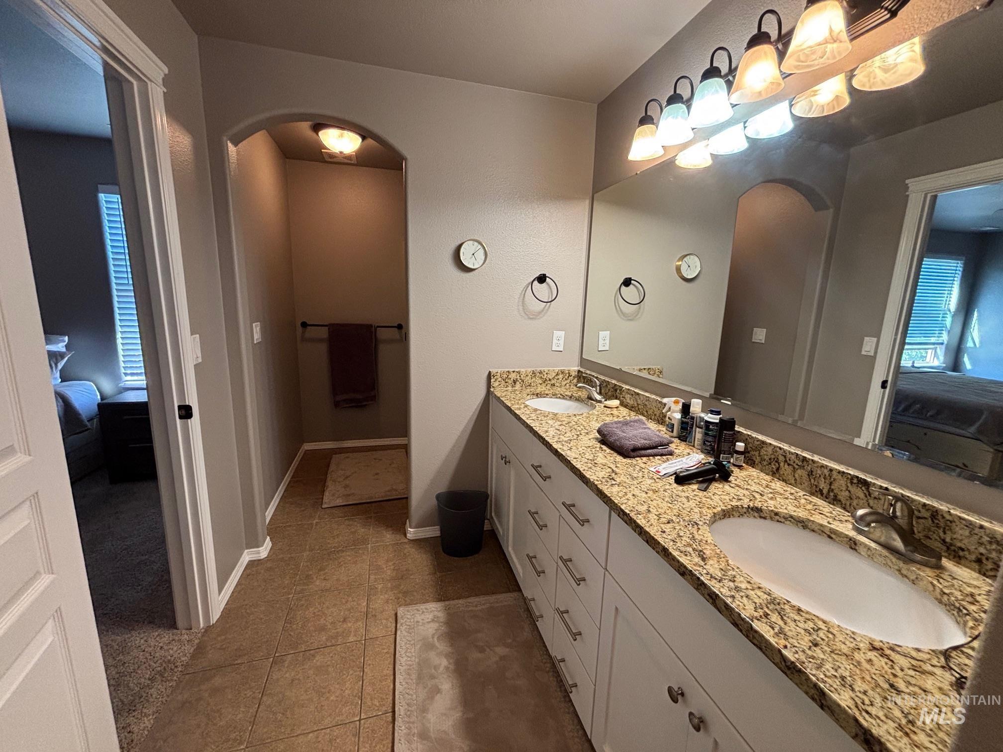 Ensuite bathroom featuring double vanity and dark tile patterned flooring