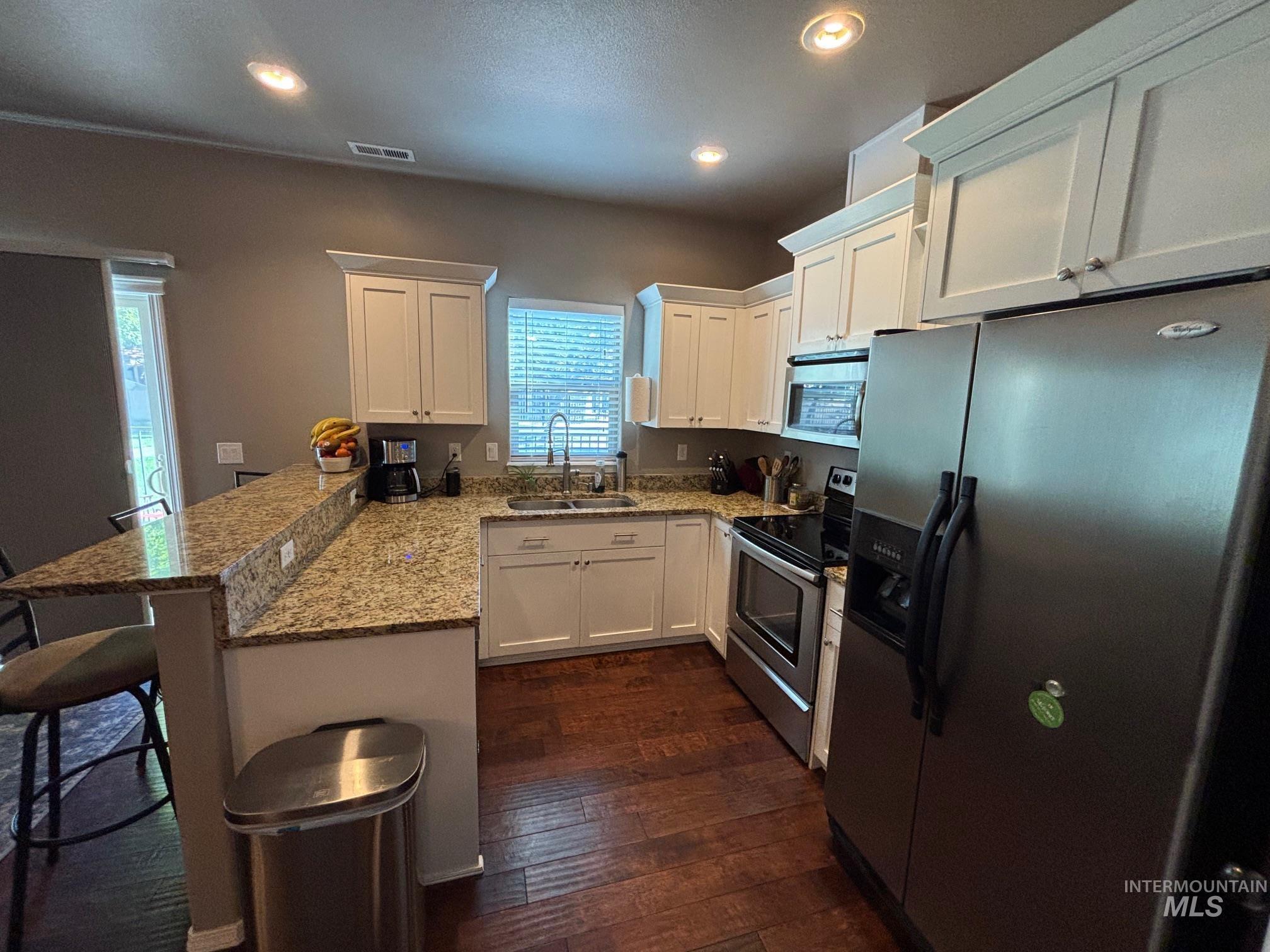 Kitchen with appliances with stainless steel finishes, a breakfast bar area, a peninsula, white cabinets, and light stone countertops