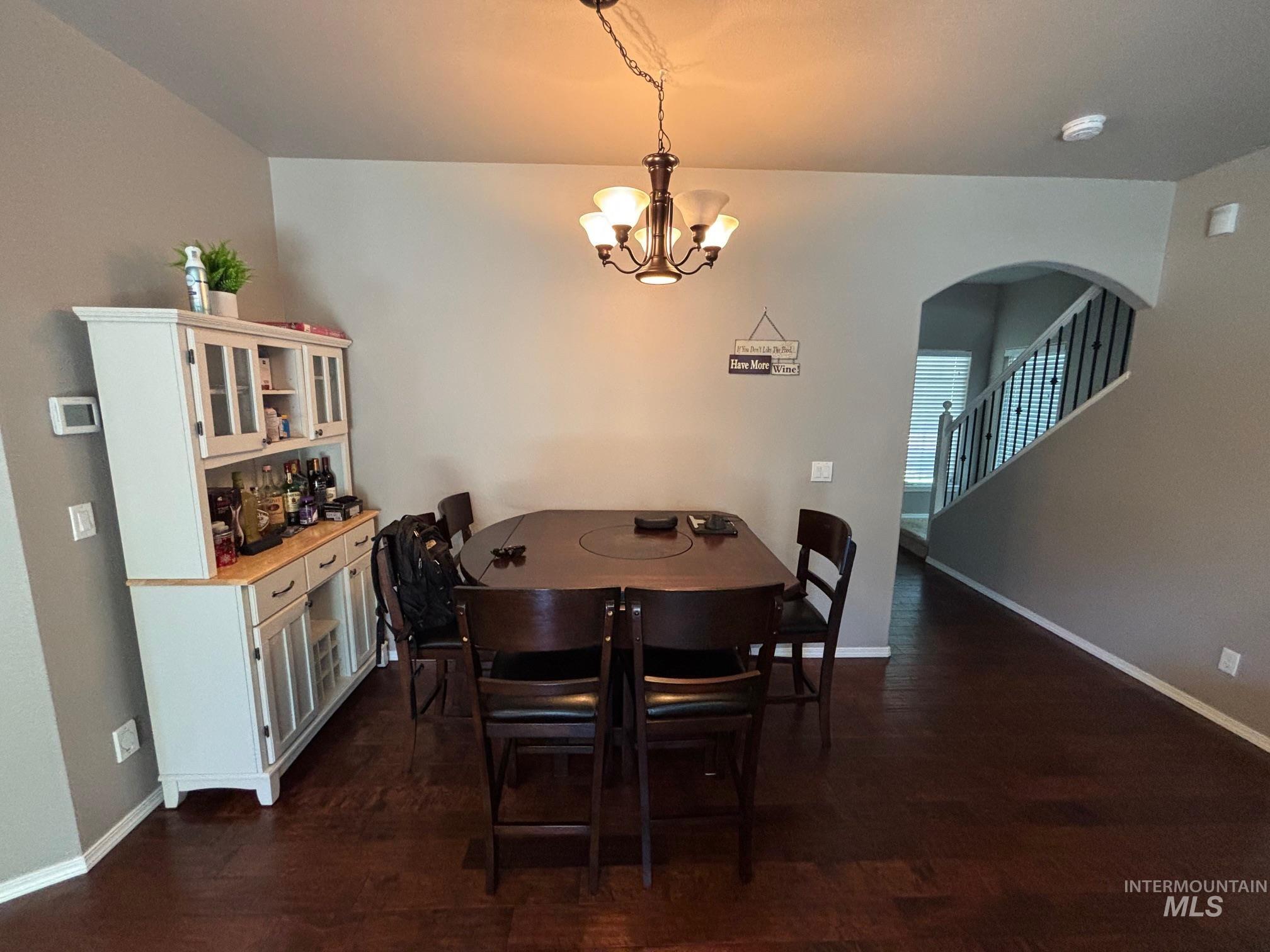 Dining space featuring dark wood-type flooring, a chandelier, and arched walkways