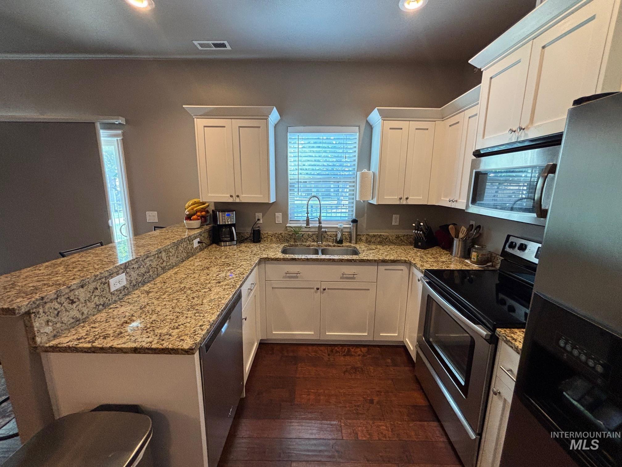 Kitchen with appliances with stainless steel finishes, light stone counters, white cabinets, and recessed lighting
