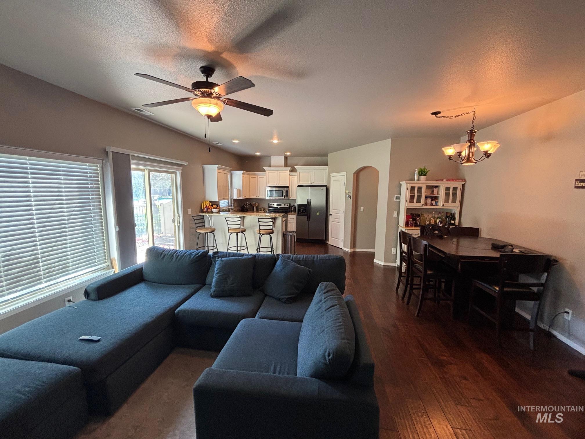Living area with arched walkways, dark wood-type flooring, a textured ceiling, a ceiling fan, and a chandelier