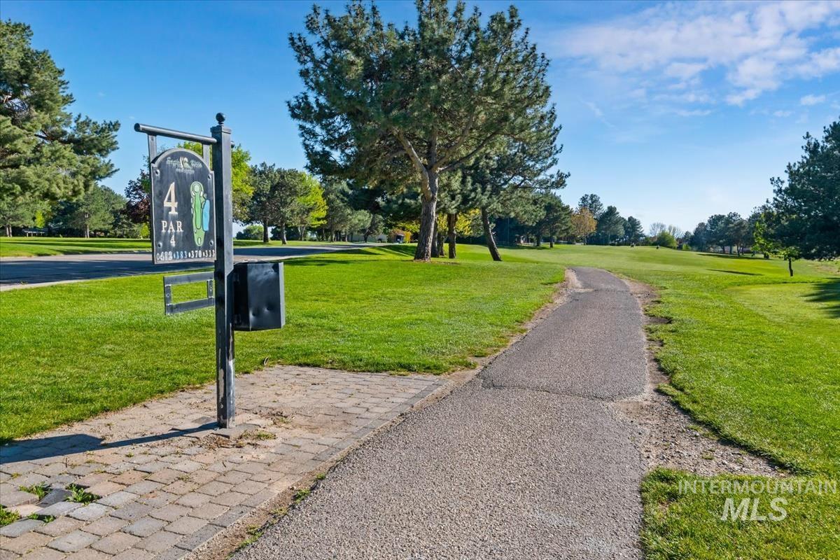 Expansive green space featuring a paved pathway, mature trees, and a golf course marker