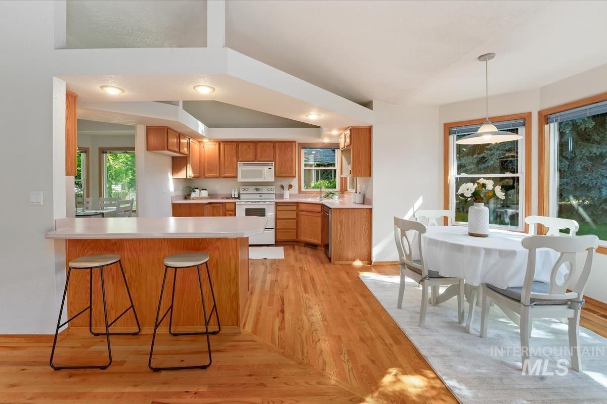 Kitchen and dining area featuring warm wood-finish flooring, light wood cabinetry, and a peninsula with countertop seating