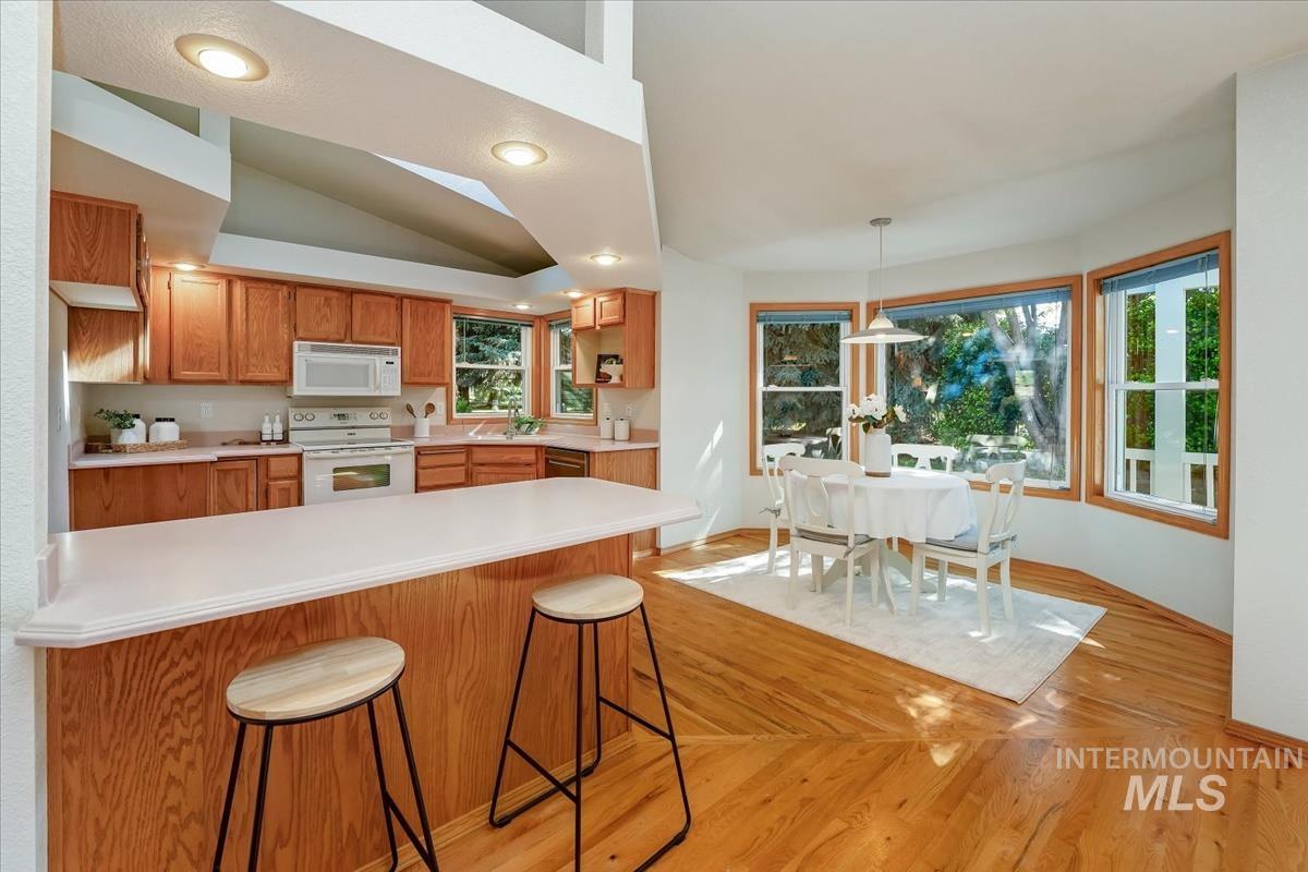 Open-concept kitchen and dining area featuring warm wood-finish cabinetry, white appliances, and a breakfast bar