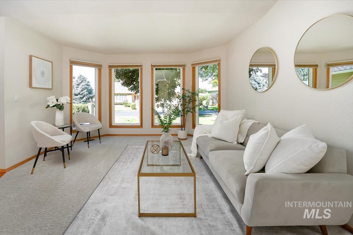 Naturally lit living area with a bay window featuring light wood trim, light neutral wall paint, and light-toned carpeting