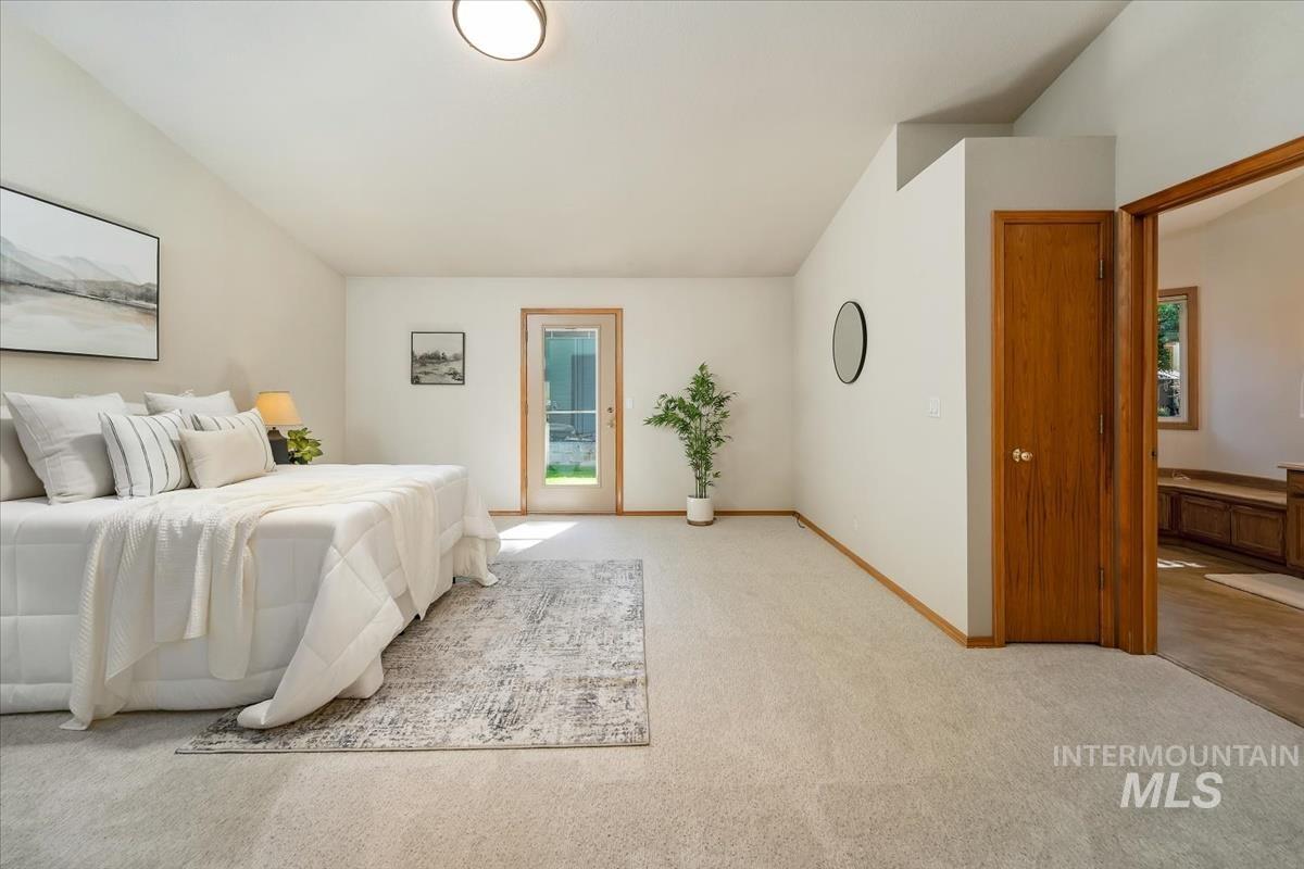 Spacious room featuring vaulted ceilings, light-toned carpeting, a full-light glass panel door, and a solid wood interior door with trim