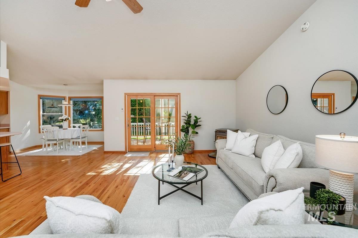 Spacious living area featuring vaulted ceilings, wood-finish flooring, and a dining area with expansive windows