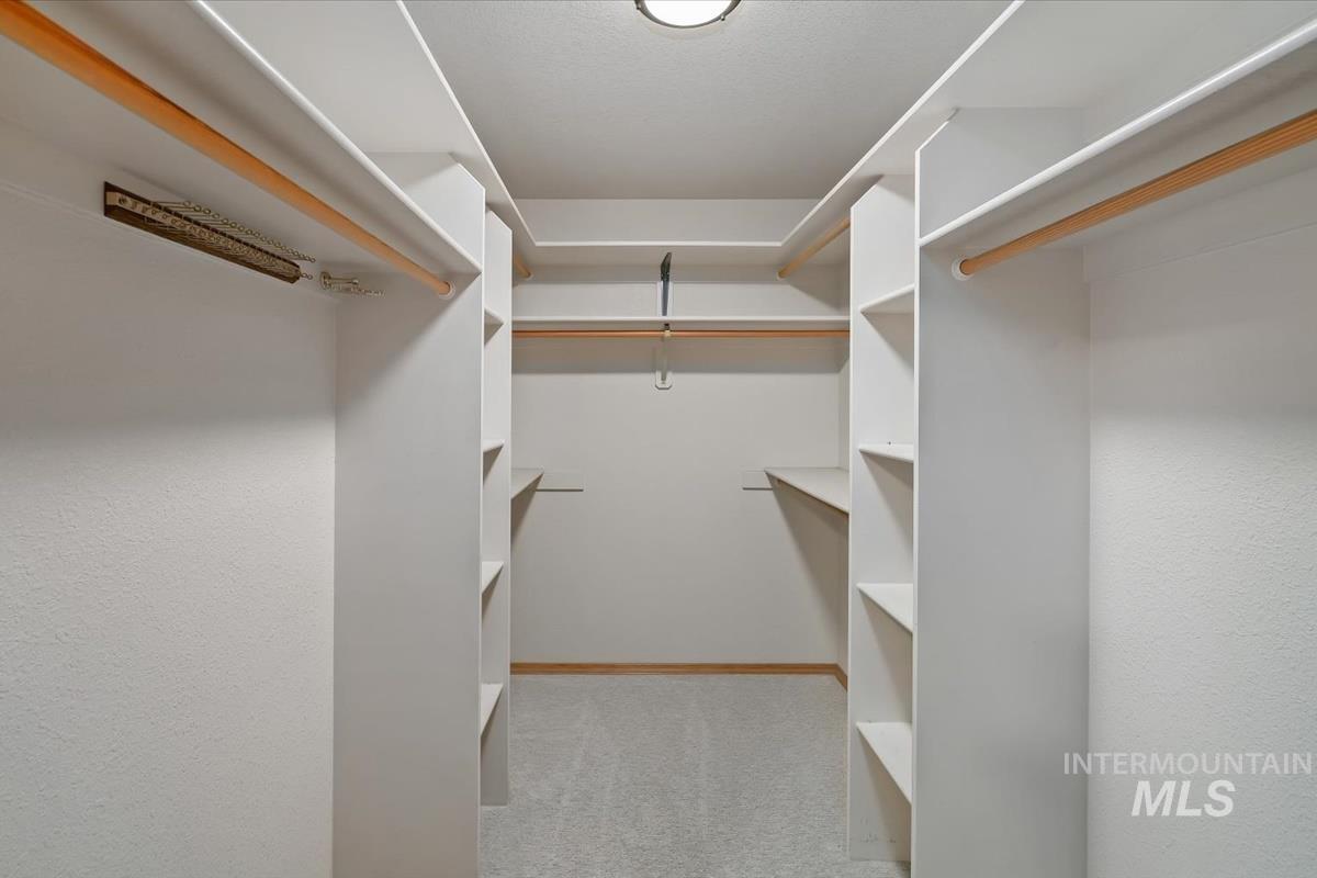 Walk-in closet with built-in shelving, multiple hanging rods, and light-toned carpeting