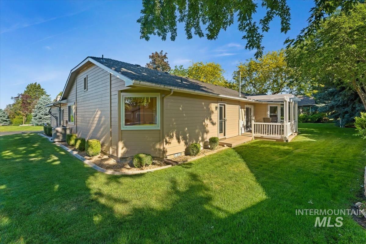 Expansive green lawn surrounds the property, featuring a covered patio with white railings, mature trees, and landscaping elements