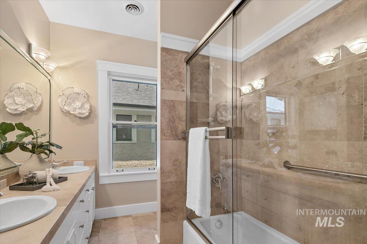 Bathroom featuring bath / shower combo with glass door and double vanity