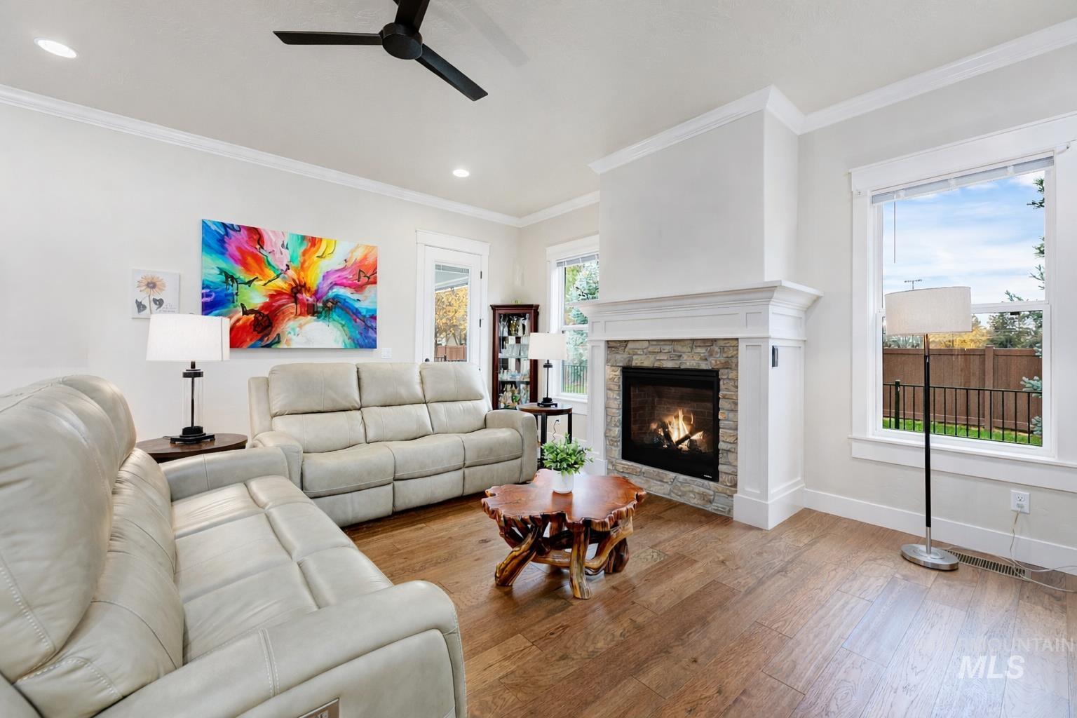 Living room featuring hardwood / wood-style floors, a ceiling fan, a stone fireplace, ornamental molding, and recessed lighting