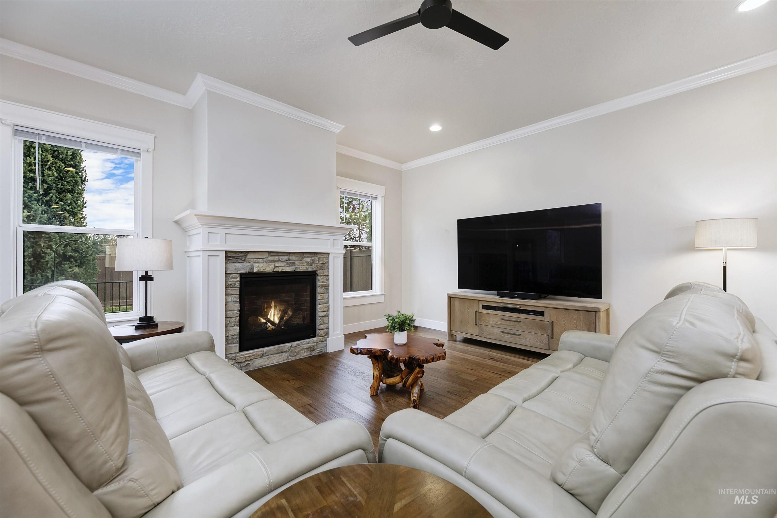 Living room featuring wood finished floors, a stone fireplace, crown molding, recessed lighting, and ceiling fan