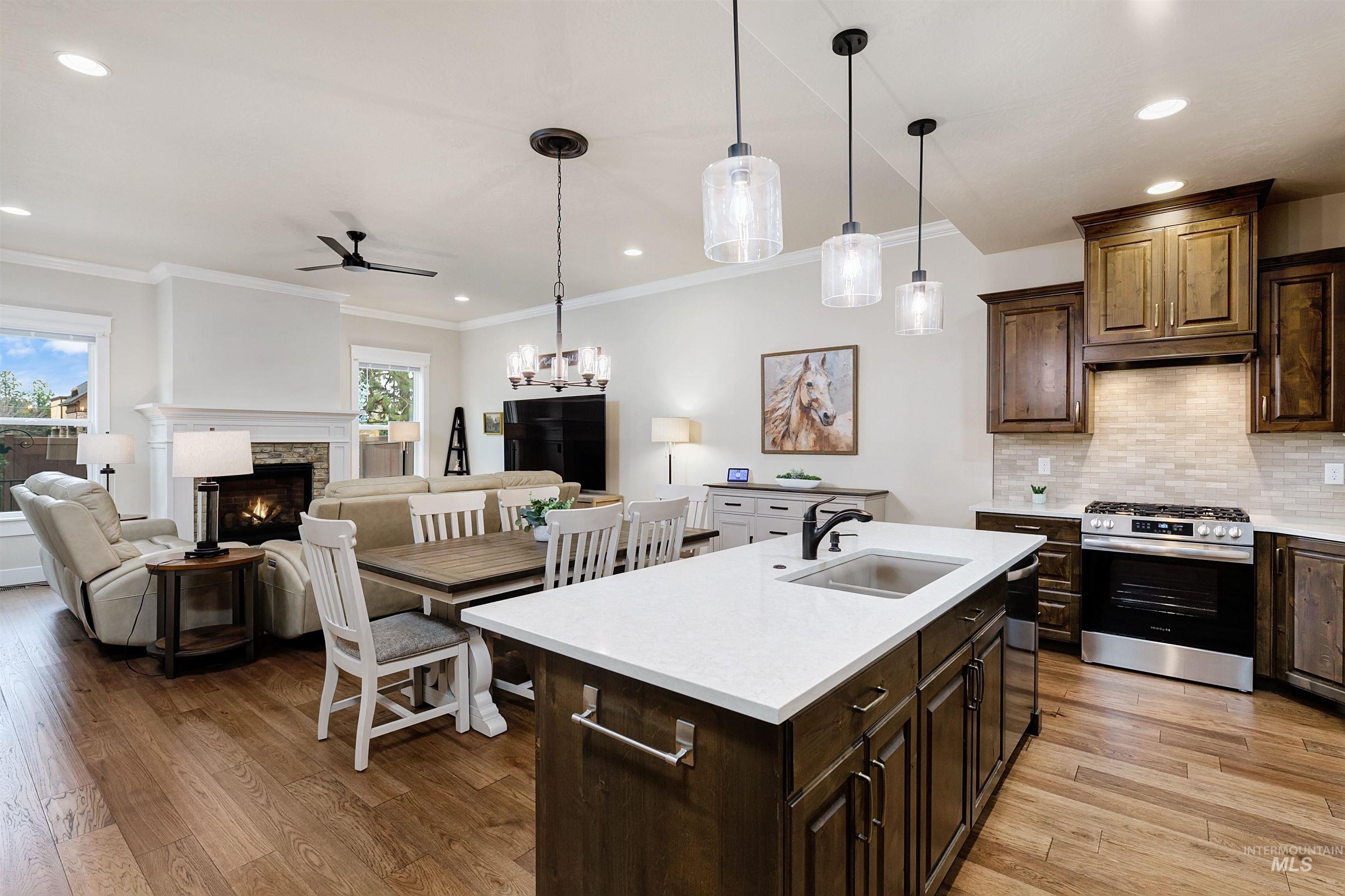 Kitchen featuring dark wood finish cabinets, gas range, hanging light fixtures, light wood-style flooring, and a fireplace