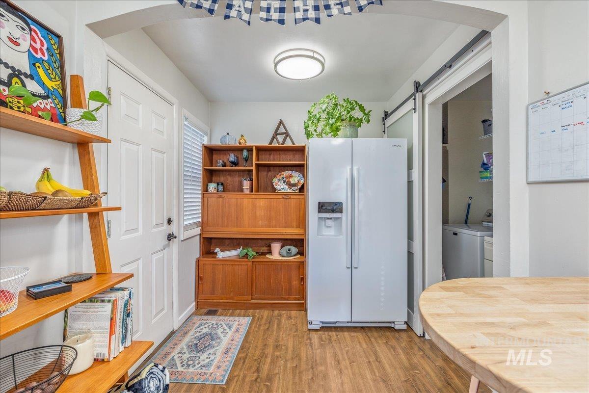 Kitchen with white fridge with ice dispenser, arched walkways, light wood-style floors, washer / dryer, and a barn door