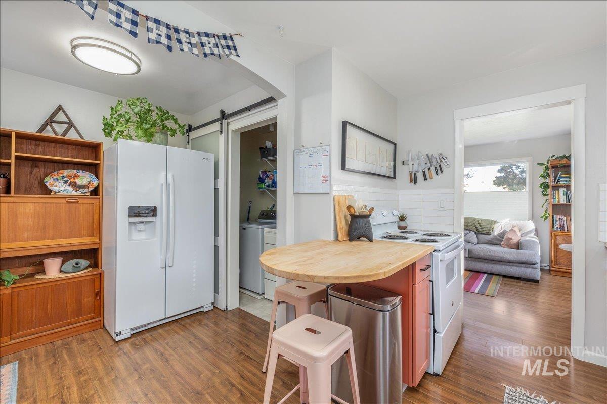 Kitchen with white appliances, a barn door, light wood-type flooring, arched walkways, and brown cabinetry