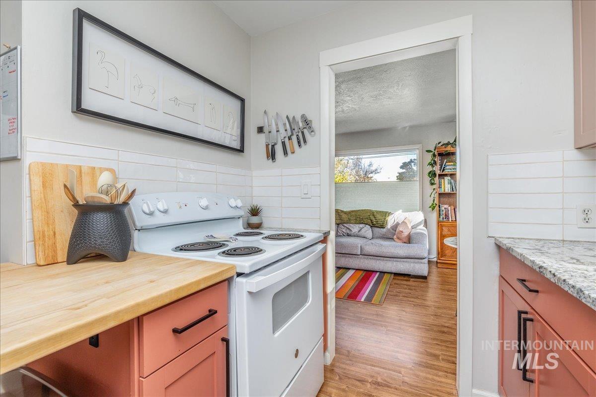 Kitchen featuring electric range, light wood-style floors, tasteful backsplash, and a textured ceiling