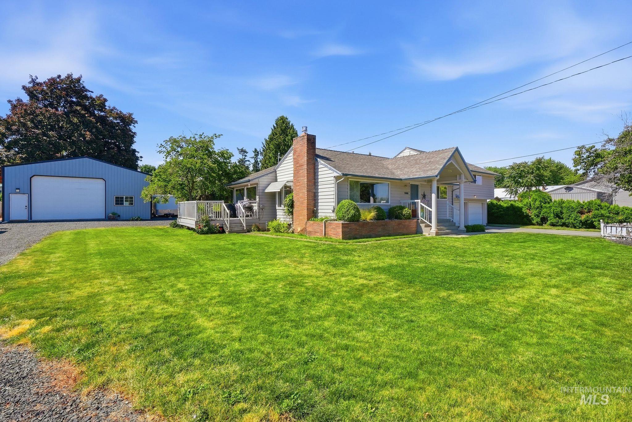 Spacious front lawn with a single-story residence, featuring a brick-clad chimney, a covered entryway, and a side deck