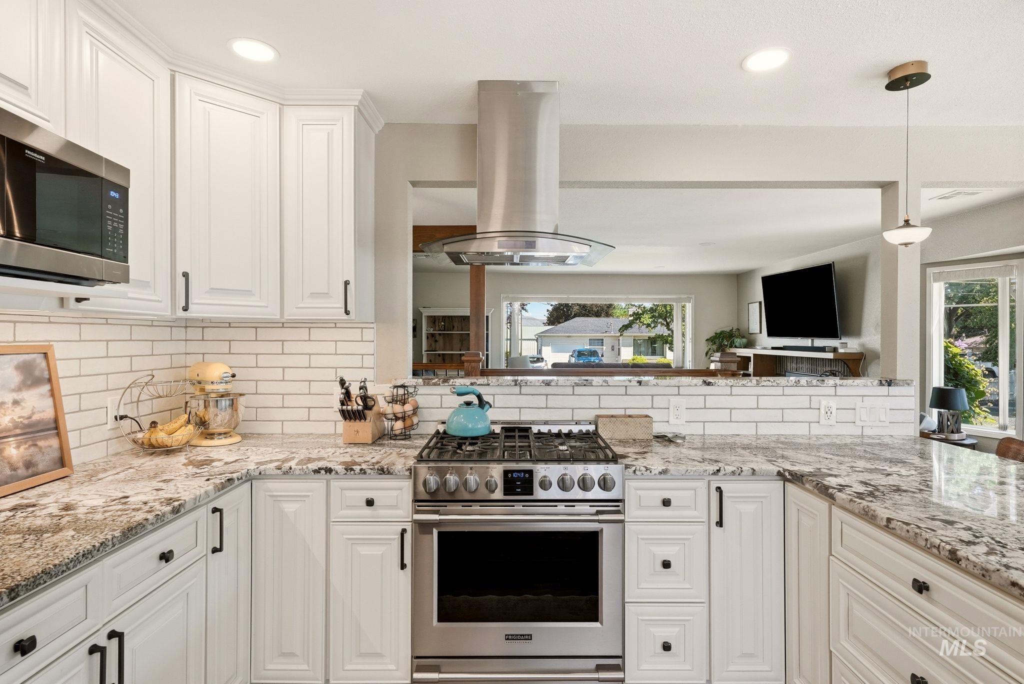 Gourmet kitchen with white cabinetry, stainless steel range and microwave, light-toned granite countertops, and white subway tile backsplash