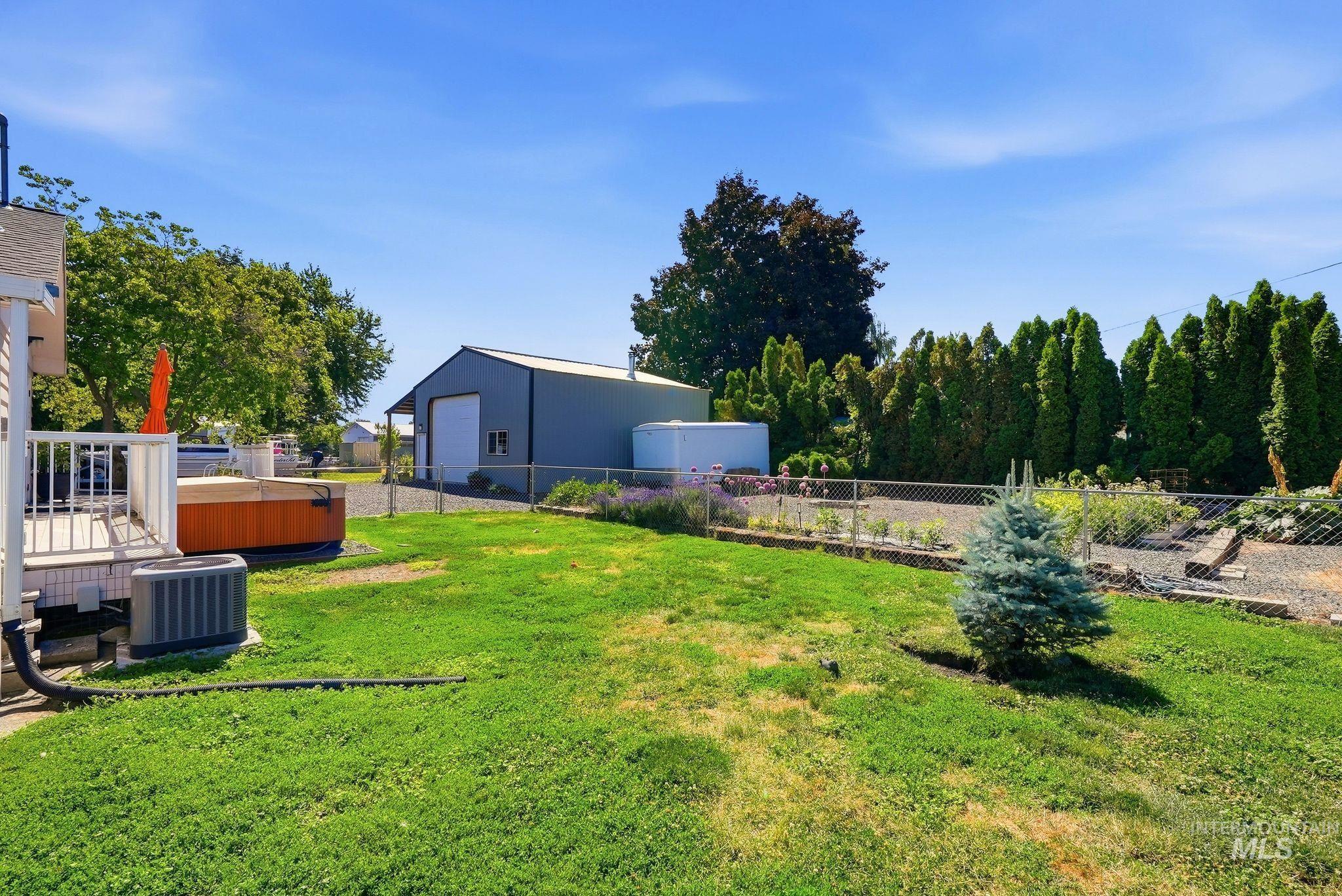 Expansive backyard featuring a lush lawn, a deck with white railings, a gravel bed, and a detached metal building with a roll-up door