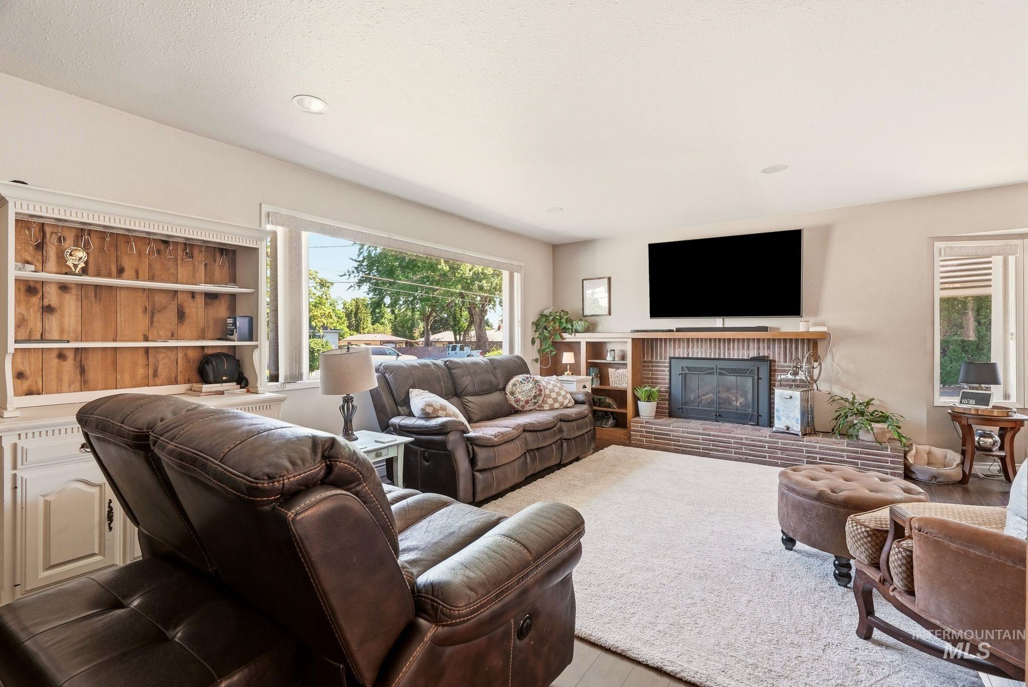 Living area featuring a brick fireplace with wood mantel, large picture window, built-in shelving, and recessed lighting